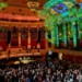 A hall full of people dancing beneath a green, shimmering ceiling